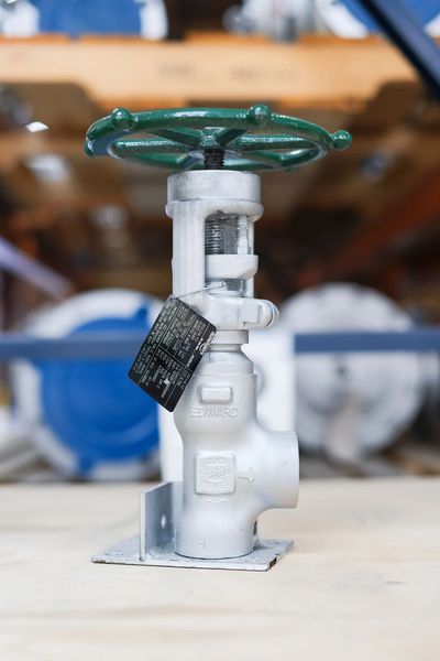 Close-up of a metallic valve with a green handwheel in an industrial setting.