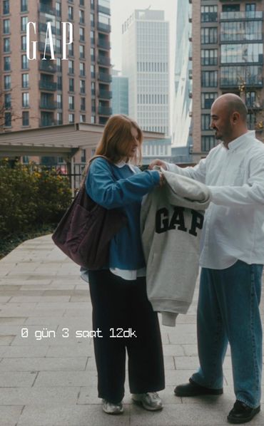 A man and woman exchanging a GAP sweatshirt in a city setting.