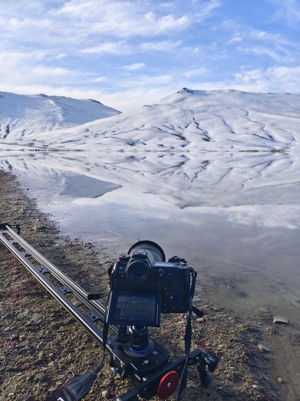 A camera on a slider capturing snowy mountain reflections in a lake.