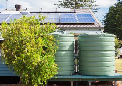 Two large green water tanks next to a house with solar panels on the roof.