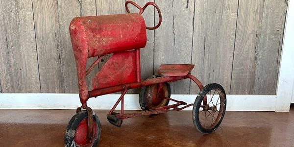 Small red antique peddle tractor on floor. 