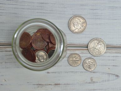 Jar of loose change and change on wood table.  Copper pennies, silver nickels, dimes, and quarters. 