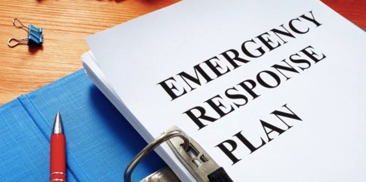 wood desk with red pen, blue binder, and white paper with black text Emergency Response Plan