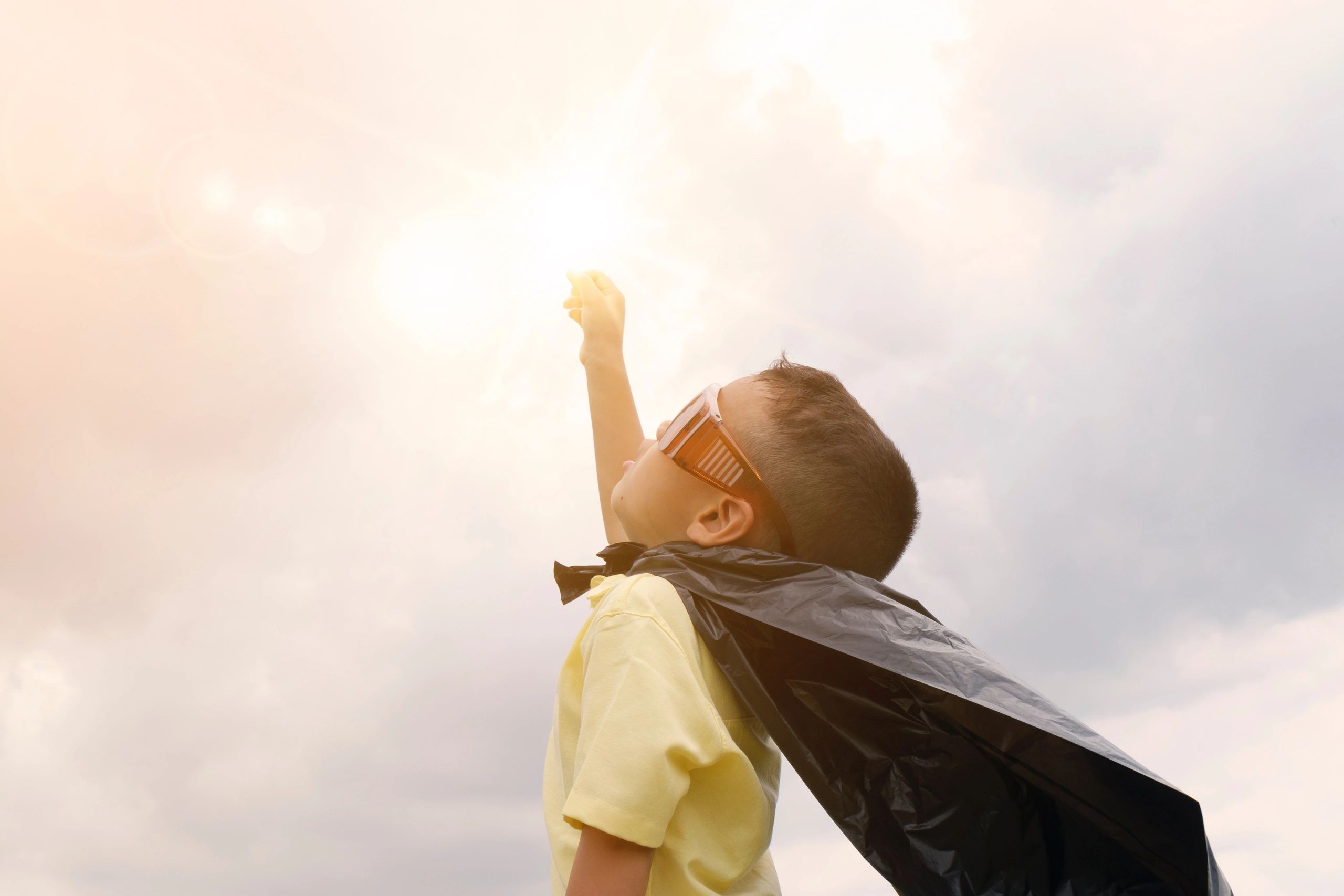 Child dressed as a superhero pointing toward sky.