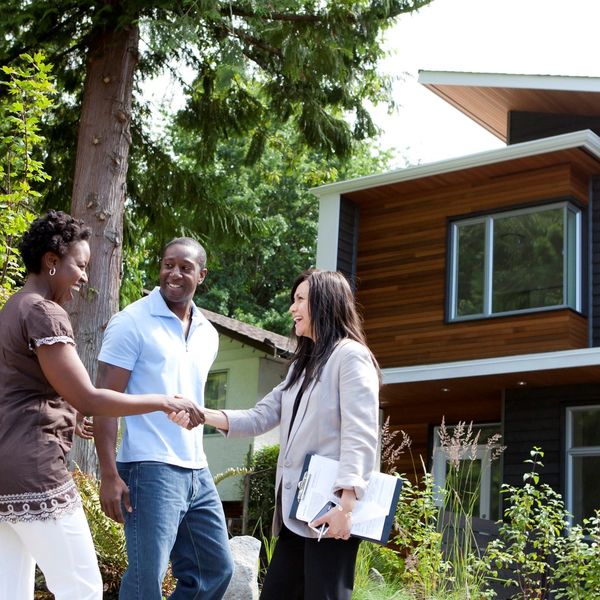 Female Real Estate agent meeting a man and woman and shaking hands with the woman in front of a home