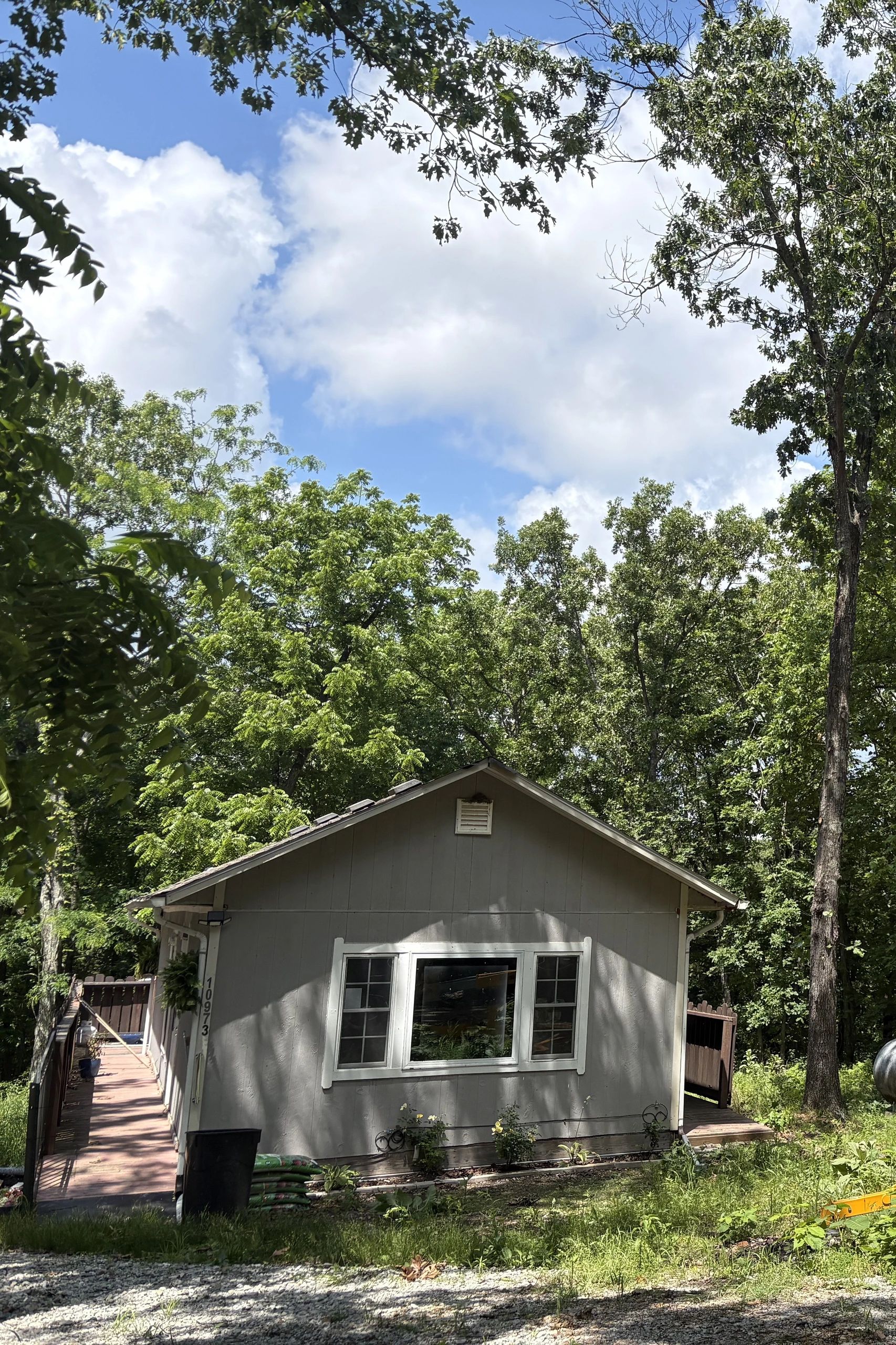 Small gray house surrounded by green trees under a blue sky.