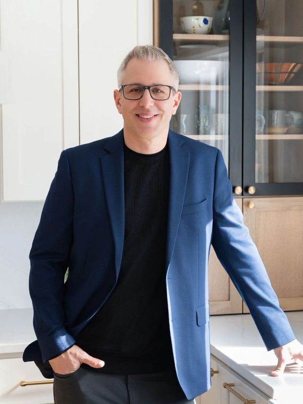 Man in blue blazer smiling in a modern kitchen.
