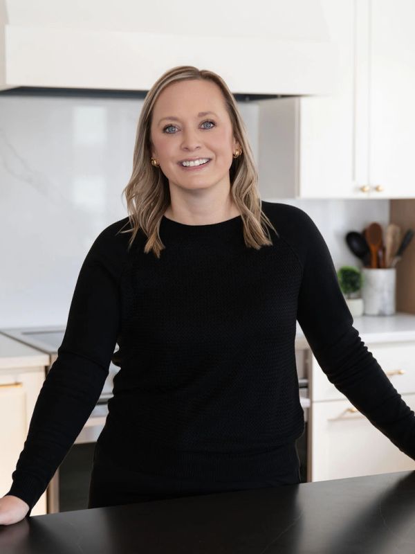 Smiling woman in black sweater standing in a modern kitchen.