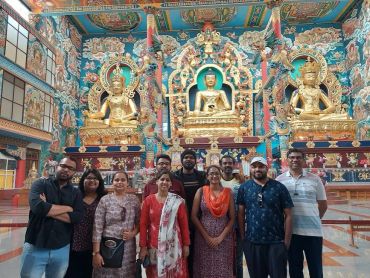 Group of people posing inside a richly decorated Buddhist temple with golden statues.