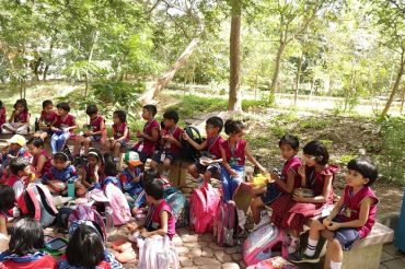 Children in school uniforms eating outdoors in a park.