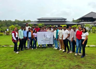 Group of young adults posing outdoors with a banner on a grassy field.