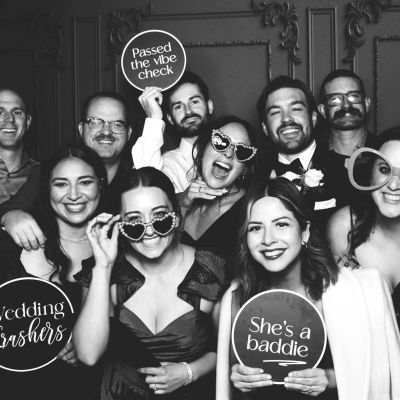 Group of friends at a wedding photo booth with fun signs and glasses.
