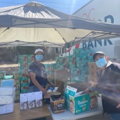 Two people wearing masks distributing baby supplies under a canopy tent.