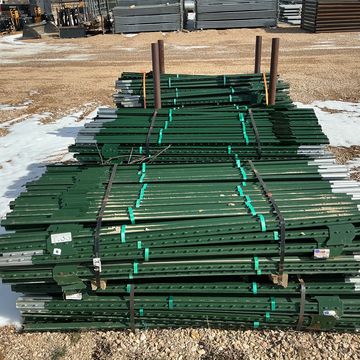 Stacks of green metal stakes bundled together outdoors on gravel.