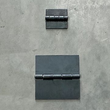 Two black metal hinges of different sizes on a gray surface.
