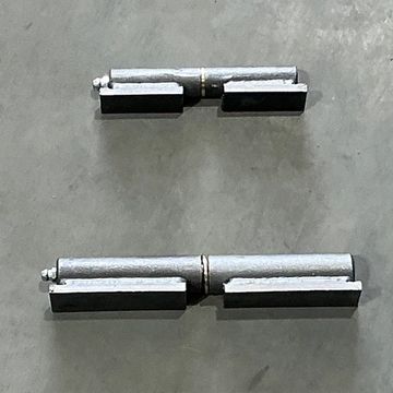 Two metal door hinges lying on a concrete surface.