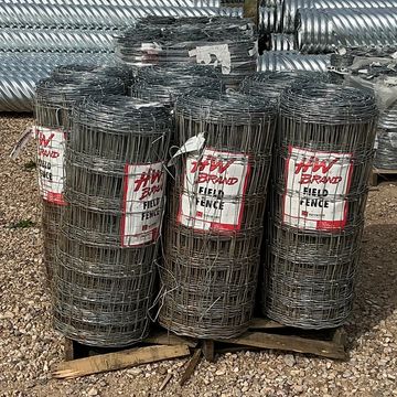 Rolls of field fence wire stacked outdoors on a pallet.