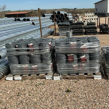 Pallets of coiled fencing wire wrapped in plastic outdoors.