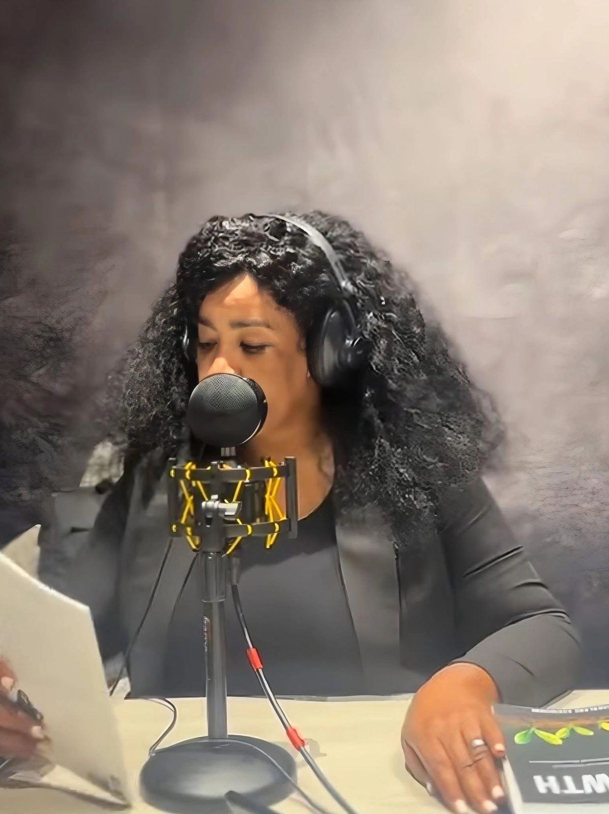 Woman recording a podcast with headphones and microphone in a studio.