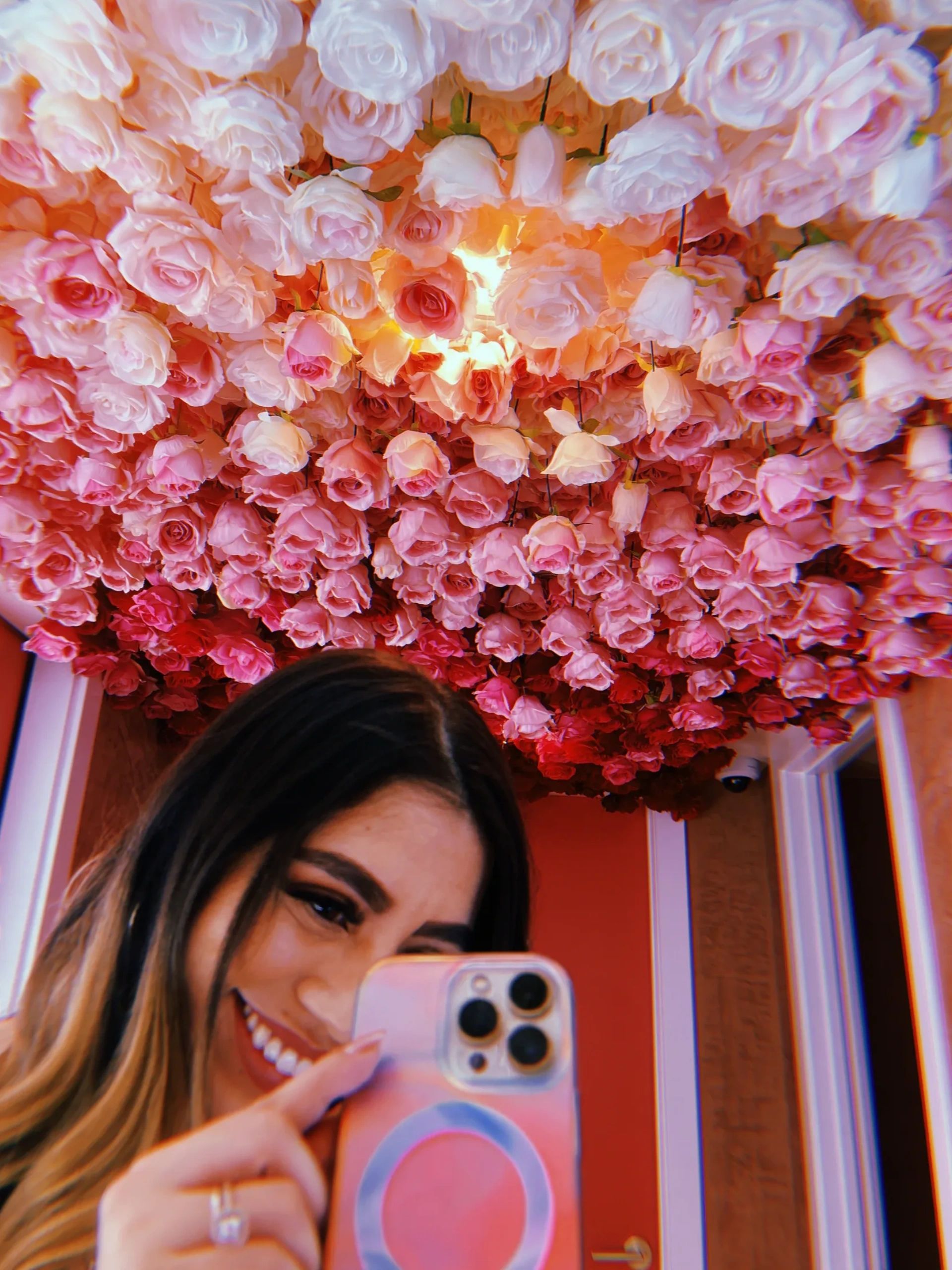 Woman taking a selfie under a ceiling covered in pink and red roses.