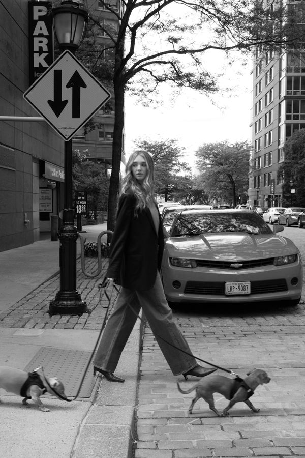 Woman walking two dogs on a city street in black and white.