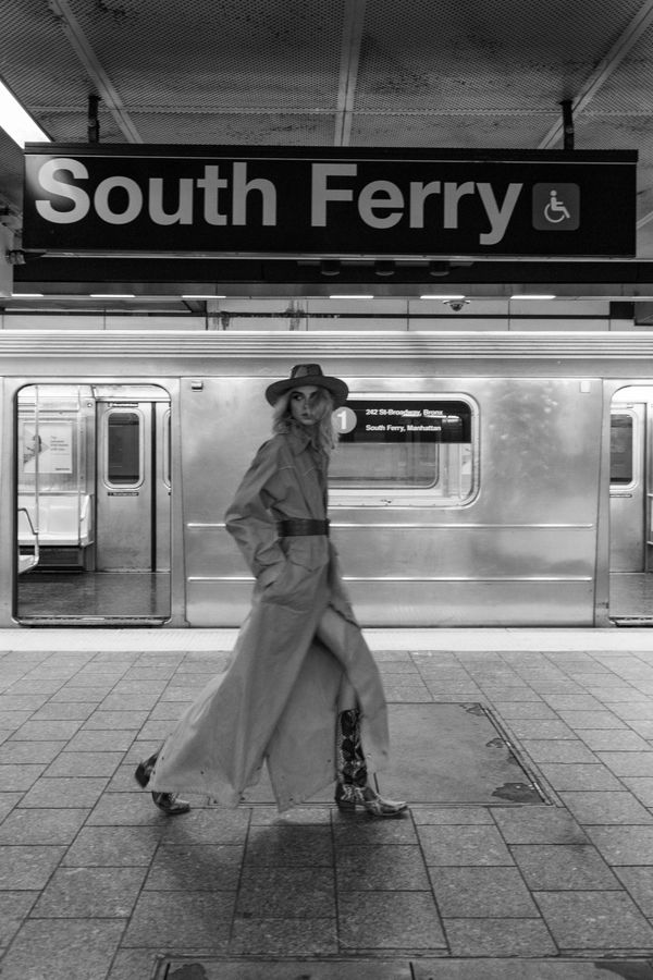 A stylish woman walks through South Ferry subway station in black and white.