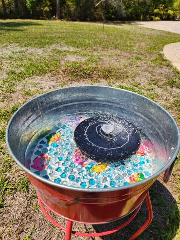 A small water fountain in a metal basin outdoors on grass.