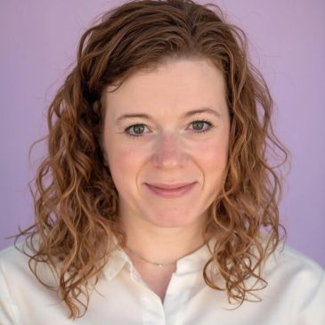 Smiling woman with curly hair against a purple background.