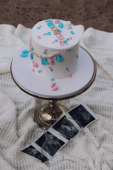 Gender reveal cake with pink and blue decorations and ultrasound images.