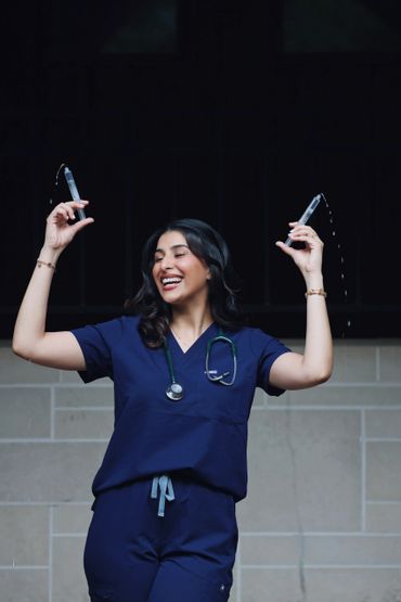 Happy nurse in blue scrubs holding syringes with water splashing out.