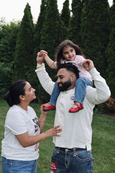 Family enjoying playful moment outdoors with daughter on father's shoulders.