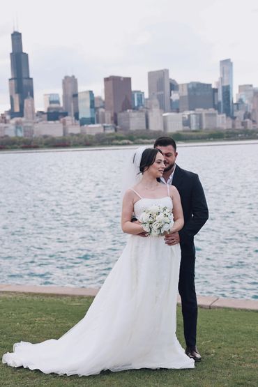 Bride and groom posing by the water with city skyline in the background.