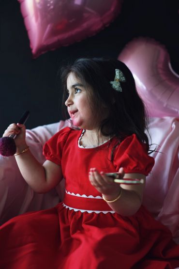 Little girl in red dress playing with makeup brush and compact.