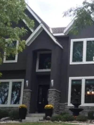 Modern two-story dark gray house with stone accents and large windows.