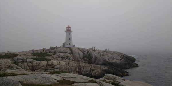 Lighthouse on rocky shore with foggy background.