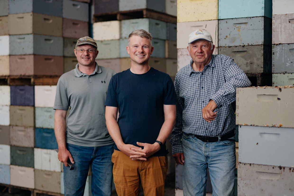Multigenerational family members standing in front of stacked beehive boxes inside a warehouse.