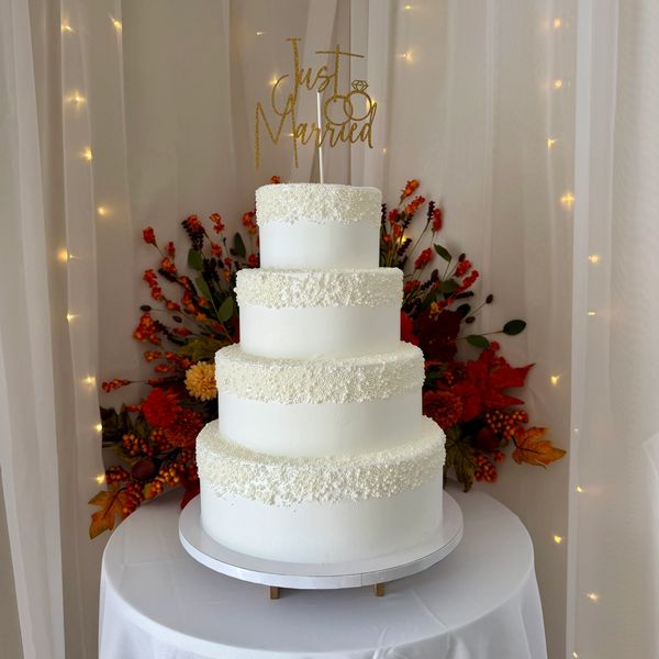 Elegant four-tier white wedding cake with "Just Married" topper.