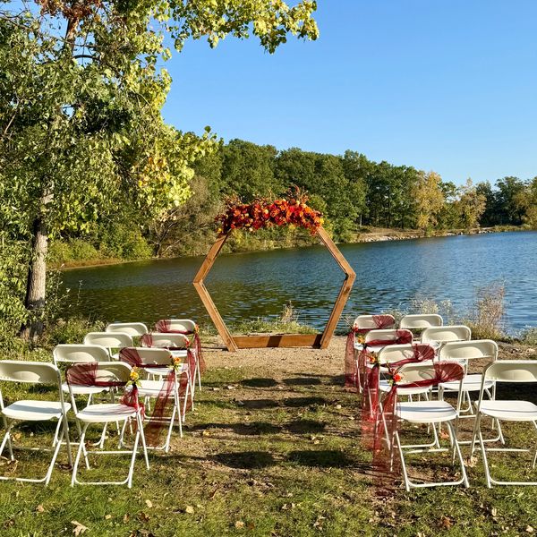 Outdoor wedding setup by a lake with decorated chairs and floral arch.