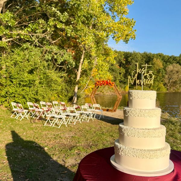 Outdoor wedding setup with cake and chairs by the lake.