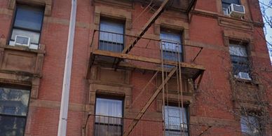 Old brick building with fire escape and window air conditioners.