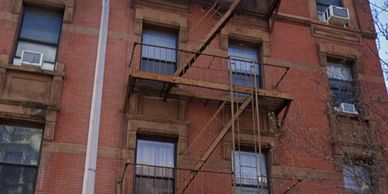 Old brick building with fire escape and window air conditioners.