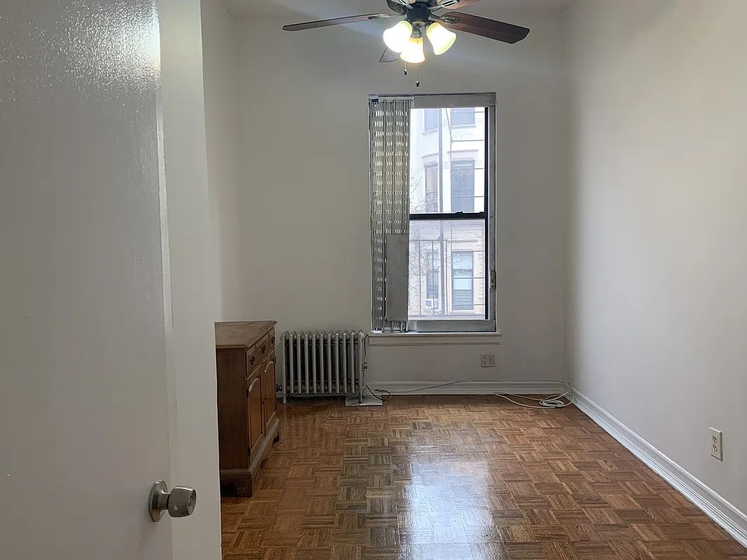 Empty room with wooden floor, ceiling fan, and window with blinds.