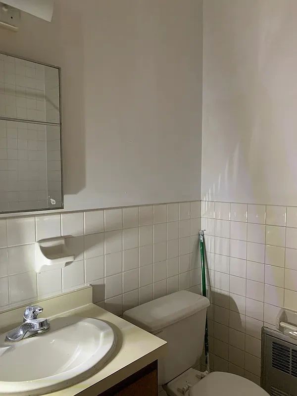 Minimalist bathroom with sink, toilet, and white tiles.