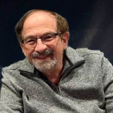 Smiling elderly man wearing glasses and a gray sweater.
