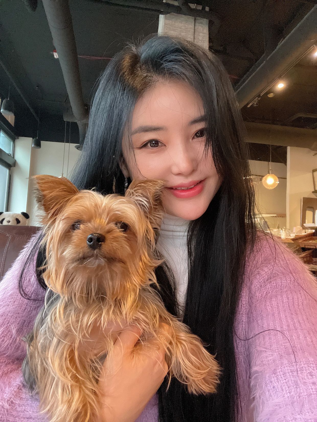 Woman holding a small dog and smiling indoors.