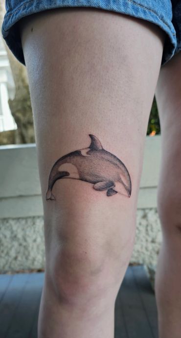 Realistic orca tattoo on the back of a person's thigh.