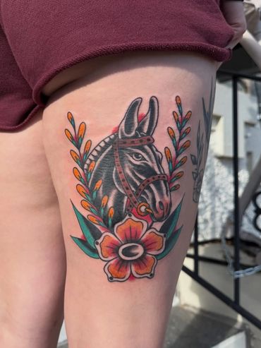 Colorful tattoo of a horse head with floral accents on a thigh.