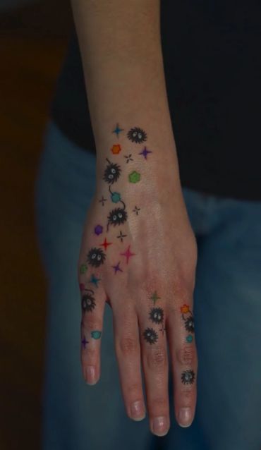 Colorful tattoo of soot sprites and stars on a hand.