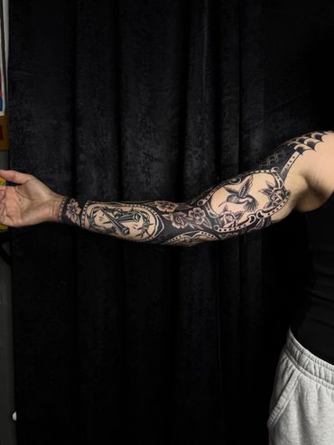 Full sleeve tattoo with intricate black and gray designs on an outstretched arm.