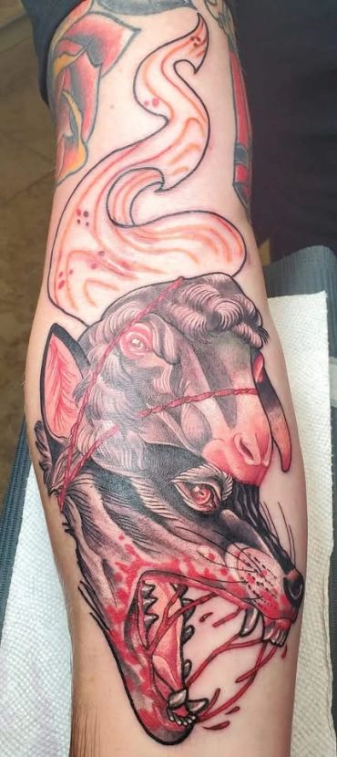 Tattoo of a fierce wolf and a sheep on a forearm.